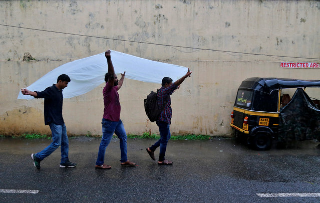 Men use a plastic sheet to cover from rain as they walk along a road in Kochi, India, May 30, 2017. (Photo by Sivaram V/Reuters)