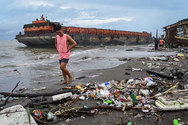 Residents walk along the shore as a barge is seen swept ashore due to Tropical Storm Yagi in Rosario, Cavite Province, on September 3, 2024. (Photo by Jam Sta Rosa/AFP Photo)