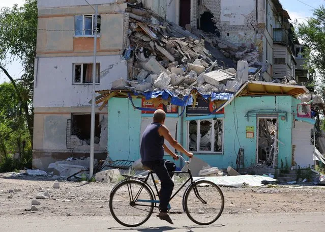 A local resident rides a bicycle past an apartment building heavily damaged during Ukraine-Russia conflict in the city of Sievierodonetsk in the Luhansk Region, Ukraine on June 30, 2022. (Photo by Alexander Ermochenko/Reuters)