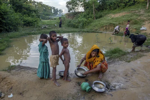 A Rohingya Muslim woman cleans utensils near a polluted pond as her children stand near her in Kutupalong refugee camp, Bangladesh, Friday, September 15, 2017. With Rohingya refugees still flooding across the border from Myanmar, those packed into camps and makeshift settlements in Bangladesh were becoming desperate for scant basic resources as hunger and illness soared. (Photo by Dar Yasin/AP Photo)