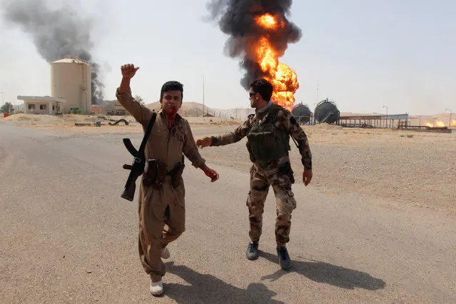 An injured member of Kurdish Peshmerga forces reacts as smoke rises after an attack at Bai Hassan oil station, northwest of Kirkuk, Iraq, July 31, 2016. Militants have attacked a gas facility and an oilfield in northern Iraq, killing five people. Gunmen on motorbikes opened fire on the facility’s guards, then killed four of its employees and planted bombs before escaping. Militants also attacked the nearby Bai Hassan oilfield, the largest in oil-rich Kirkuk province, killing an engineer and causing a major fire. (Photo by Ako Rasheed/Reuters)