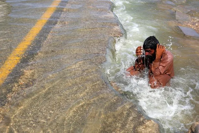 A displaced man cools off to avoid heat on flooded highway, following rains and floods during the monsoon season in Sehwan, Pakistan on September 16, 2022. (Photo by Akhtar Soomro/Reuters)