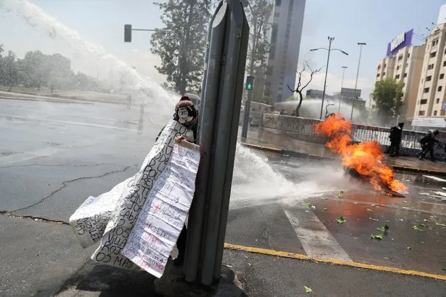 A person takes cover from a police water cannon as demonstrators take part in a rally on the third anniversary of the protests and riots that rocked the country in 2019, in Santiago, Chile on October 18, 2022. (Photo by Ivan Alvarado/Reuters)