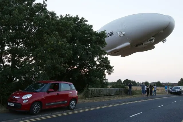 The Hybrid Air Vehicles HAV 304 Airlander 10 hybrid airship is seen in the air over a road on its maiden flight from Cardington Airfield near Bedford, north of London, on August 17, 2016. The Hybrid Air Vehicles 92-metre long, 43.5-metre wide Airlander 10, billed as the world's longest aircraft, lifted off for the first time from an airfield north of London. The Airlander 10 has a large helium-filled fabric hull and is propelled by four turbocharged diesel engines. According to the company it can stay airborne for up to five days at a time if manned, and for over 2 weeks unmanned with a cruising speed of just under 150 km per hour and a payload capacity of up to 10,000 kg. (Photo by Justin Tallis/AFP Photo)