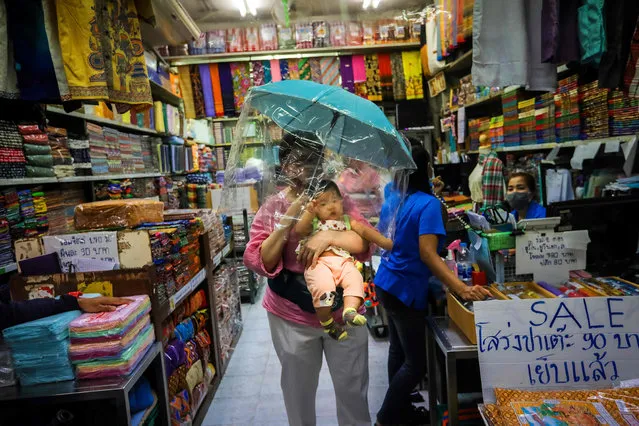 In this file photo taken on March 24, 2020 a woman carries a baby under an umbrella with a plastic covering as a preventive measure against the spread of the COVID-19 novel coronavirus at a market in Bangkok. Thailand is set to declare a state of emergency to slow the spread of a virus which has killed four in the kingdom, its premier said March 24. (Photo by Vivek Prakash/AFP Photo)