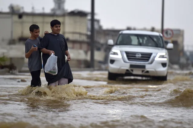 Youthd walk in a flooded street following heavy rains in the Saudi coastal city of Jeddah on November 24, 2022 which delayed flights, forced school suspensions and closed the road to Mecca, Islam's holiest city. Jeddah, a city of roughly four million people positioned on the Red Sea, is often referred to as the “gateway to Mecca”, where millions perform the hajj and umrah pilgrimages each year. Winter rainstorms and flooding occur almost every year in Jeddah, where residents have long decried poor infrastructure. (Photo by Amer Hilabi/AFP Photo)