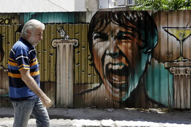 A man passes graffiti in Athens, Tuesday, July 21, 2015. (Photo by Thanassis Stavrakis/AP Photo)