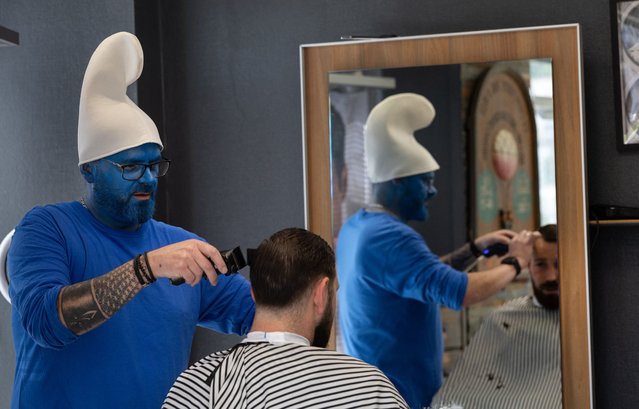 A hairdresser wearing a smurf (schtroumpf) costume works on a client on the sidelines of an attempt to break the world record for the largest gathering of Smurfs, in Landerneau, western France, on May 17, 2025. Landerneau on May 17 attempts to break the world record for the largest Smurfs gathering, a record held by Lauchringen in Germany, after two failed attempts over five years. (Photo by Fred Tanneau/AFP Photo)