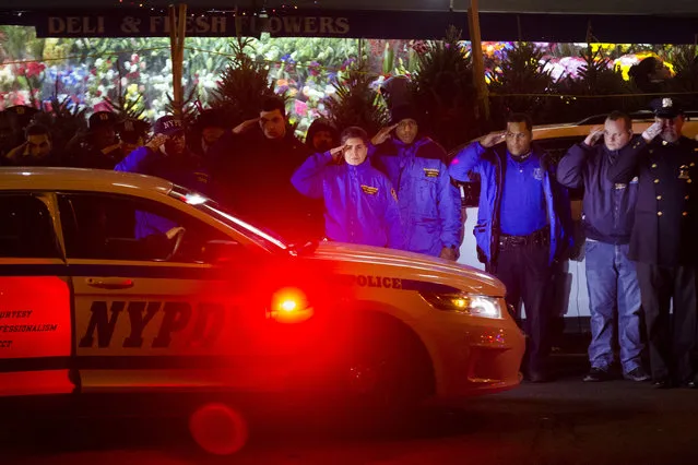 Mourners stand at attention as the bodies of two fallen NYPD police officers are transported from Woodhull Medical Center, Saturday, December 20, 2014, in New York. An armed man walked up to two New York Police Department officers sitting inside a patrol car and opened fire Saturday afternoon, killing one and critically wounding a second before running into a nearby subway station and committing suicide, police said. (Photo by John Minchillo/AP Photo)