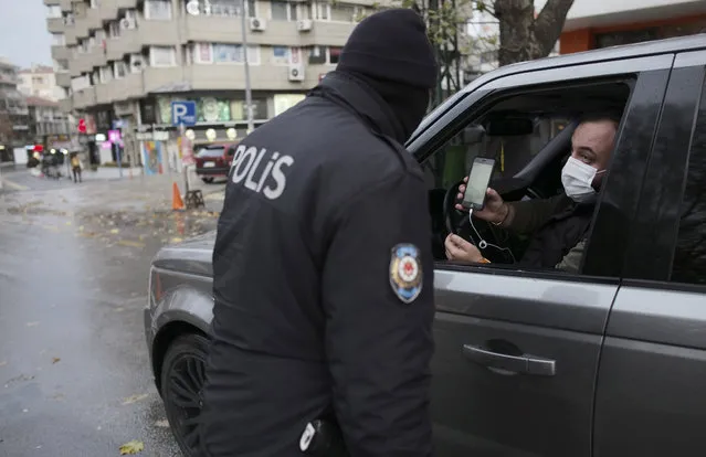 A man wearing a mask to help protect against the spread of coronavirus, shows a document as a police officer checks IDs during a two-day weekend curfew, in Ankara, Turkey, Sunday, December 13, 2020. Turkey imposed a two-day curfew from Friday evening to Monday morning as the total number of COVID-19 infections in Turkey tripled to almost 1,750,000 on Thursday after the government retrospectively corrected its count. (Photo by Burhan Ozbilici/AP Photo)