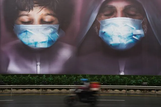 In this Wednesday, April 15, 2020 file photo, a motorcycle delivery man rides past a billboard urging people to stay home over the coronavirus pandemic in Dubai, United Arab Emirates. Wealthier Western countries are considering how to ease lockdown restrictions and start taking gradual steps toward reviving business and daily life. But many developing countries, particularly in the Middle East and Africa, can hardly afford the luxury of any misstep. (Photo by Jon Gambrell/AP Photo/File)