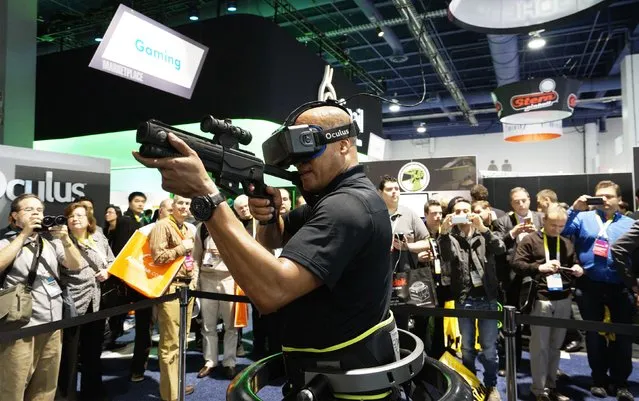 A man wearing an Oculus VR headset demonstrates a first person shooter game in a Virtuix Omni virtual reality system at the International Consumer Electronics show (CES) in Las Vegas, Nevada January 6, 2015. Wearing special shoes with sensors, the player can actually run in the game. (Photo by Rick Wilking/Reuters)