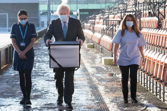 Prime Minister Boris Johnson carries Oxford/AstraZeneca Covid 19 vaccines for distribution during a visit to Barnet FC's ground at The Hive, north London, which is being used as a coronavirus vaccination centre on January 25, 2021. (Photo by Stefan Rousseau/Pool via AFP Photo)