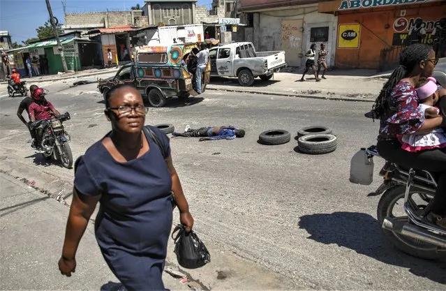 A woman walks past the body of a man, killed by unknown gunmen, lying in the middle of a road, in Port-au-Prince, Haiti, Thursday, April 20, 2023. (Photo by Joseph Odelyn/AP Photo)