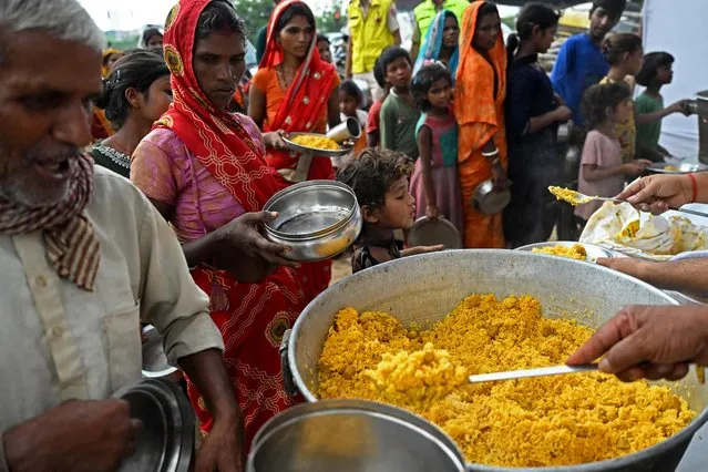 People stand in queues to receive food at a temporary shelter after Yamuna River overflowed due to heavy monsoon rains in New Delhi on July 12, 2023. (Photo by Arun Sankar/AFP Photo)