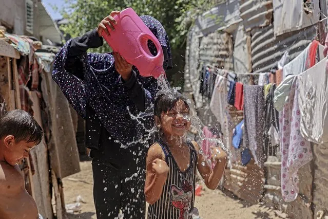 A Palestinian mother pours water over her child amidst soaring temperatures and power cuts in Gaza City on July 18, 2023. (Photo by Mohammed Abed/AFP Photo)