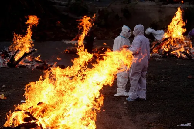 Relatives wearing personal protective equipment (PPE) walk amid burning funeral pyres as they perform last rites for covid-19 victims in Bhopal, India, 15 April 2021. A weekend curfew was announced on 15 April in Delhi and many other states as India recorded its highest daily spike of COVID-19 cases on 14 April with around 200,000 new infections in 24 hours. (Photo by Sanjeev Gupta/EPA/EFE)
