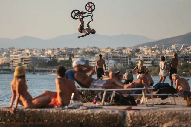 Professional BMX rider George Davoutian performs with his BMX bicycle after taking off from a ramp that was set up by the sea for jumping into the water to deal with the heatwave in the most fun way during a small event organized by the Gutlessbmx Crew at Kavouri beach, near Athens, Greece, 27 August 2023. (Photo by George Vitsaras/EPA)
