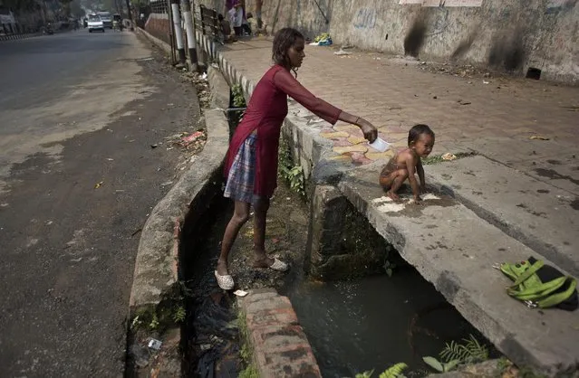Shikha Roy, an Indian woman who lives on the pavement baths her one and half year old child Twinkle using water from a leaking pipe as it flows through a drain beneath on World Water Day in Gauhati, India, Sunday, March 22, 2015. (Photo by Anupam Nath/AP Photo)