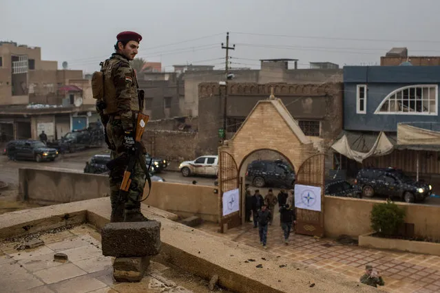 A soldier stands watch on the rooftop as people arrive for the Christmas Day mass at Mar Hanna church in Qaraqosh on December 25, 2016 in Mosul, Iraq. The predominantly Christian towns of Bartella and Qaraqosh on the outskirts of Mosul were recently liberated from ISIL as part of the Mosul offensive. The towns were heavily damaged and churches burned and defaced while under ISIL control. Christian communities around Mosul are celebrating Christmas Day as the Mosul offensive continues. (Photo by Chris McGrath/Getty Images)