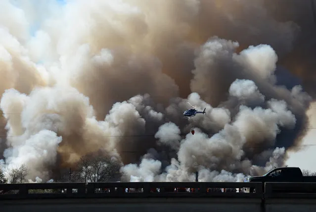 A helicopter flies past plumes of smoke during firefighting efforts on a train trestle parallel to Interstate 10 near the Bonnet Carre Spillway, west of New Orleans on Saturday, February 13, 2016. A CN Railway spokesman says it typically carries four to eight freight trains a day, plus one passenger train in each direction. (Photo by Jeff Strout/AP Photo)