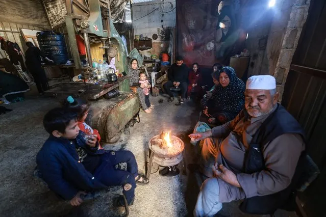 Members of a Palestinian family who fled Gaza City to Khan Yunis and had to recently flee to Rafah in the southern Gaza Strip, gather around a small fire, inside a workshop where they found temporary shelter, on December 9, 2023, amid continuing battles between Israel and the militant group Hamas. – Israel pressed its offensive against Hamas militants in Gaza on December 9, after the United States blocked an extraordinary UN bid to call for a ceasefire in the two-month war. (Photo by Mohammed Abed/AFP Photo)