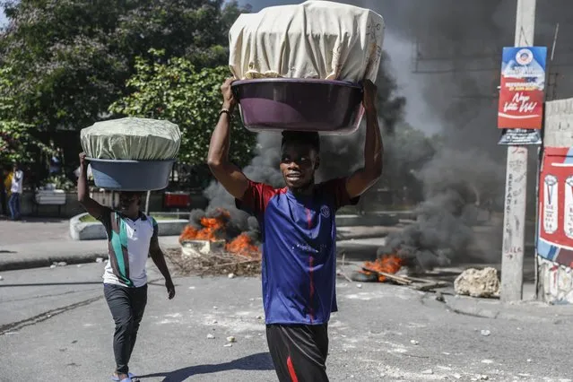 Street vendors walk past a burning road block set by anti-government protesters in Port-au-Prince, Haiti, Thursday, October 21, 2021. Demonstrators decry a severe fuel shortage and a spike in insecurity as they demanded that Prime Minister Ariel Henry step down. (Photo by Joseph Odelyn/AP Photo)