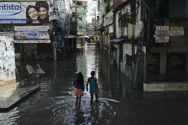 In this Wednesday, April 10, 2019 photo, children wade through a flooded street in Rio de Janeiro, Brazil. Heavy rains killed at least 10 people and left a trail of destruction in Rio de Janeiro on Tuesday, raising questions about the city's preparedness to deal with recurring extreme weather. (Photo by Leo Correa/AP Photo)