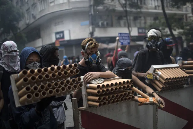 Demonstrators holding fireworks as weapons stand behind a barricade during clashes with police as they protest the state government in Rio de Janeiro, Brazil, Thursday, February 9, 2017. The protesters are denouncing a proposal to privatize the state's water and sewage company. (Photo by Felipe Dana/AP Photo)