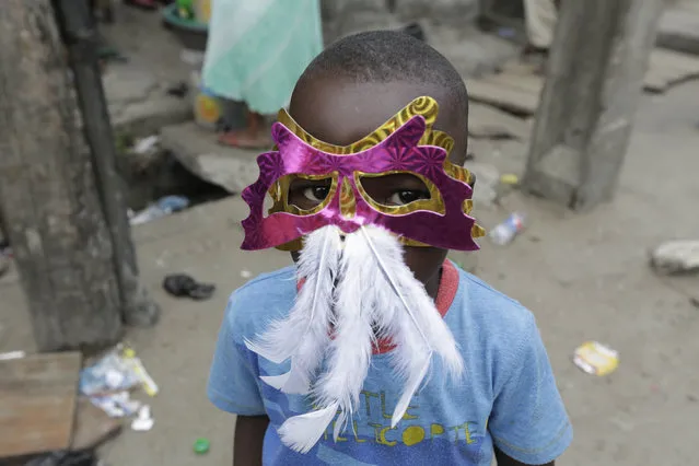 A child wears a mask and watches performers dance through the street during the Lagos Carnival, Nigeria, Saturday May 9, 2015. (Photo by Sunday Alamba/AP Photo)