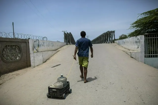 A man pulls a crate on wheels with empty bottles as he fetches potable water in Machurucuto, Venezuela, Sunday, May 5, 2019. (Photo by Rodrigo Abd/AP Photo)