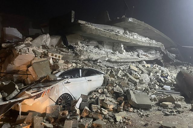 A car is seen under the wreckage of a collapsed building, in Azmarin town, in Idlib province, northern Syria, Monday, February 6, 2023. A powerful earthquake has caused significant damage in southeast Turkey and Syria and many casualties are feared. Damage was reported across several Turkish provinces, and rescue teams were being sent from around the country. (Photo by Ghaith Alsayed/AP Photo)