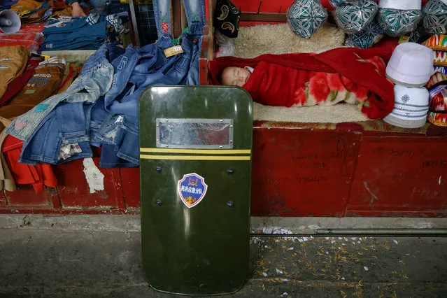 A child sleeps as a riot shield leans on a stall at the bazaar in Hotan, Xinjiang Uighur Autonomous Region, China, March 21, 2017. (Photo by Thomas Peter/Reuters)