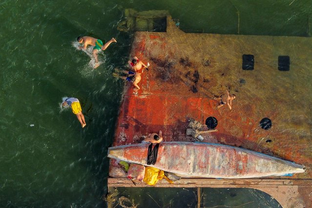 This aerial vew shows children swimming next to a sunken vessel in the Shatt al-Arab river, formed at the confluence of the Tigris and Euphrates rivers, in Iraq's southern city of Basra on May 25, 2024. (Photo by Hussein Faleh/AFP Photo)
