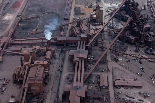 Burns Harbor, Indiana, US. The iron ore, coke fuel and limestone flux at upper left are processed and blended in the buildings connected by conveyor belt housings in the foreground. Then they are transported to the tops of the two tall blast furnaces at right via the long diagonal conveyors and charged into the furnaces for smelting to molten iron. (Photo by J. Henry Fair/Industrial Scars/Papadakis Publisher)