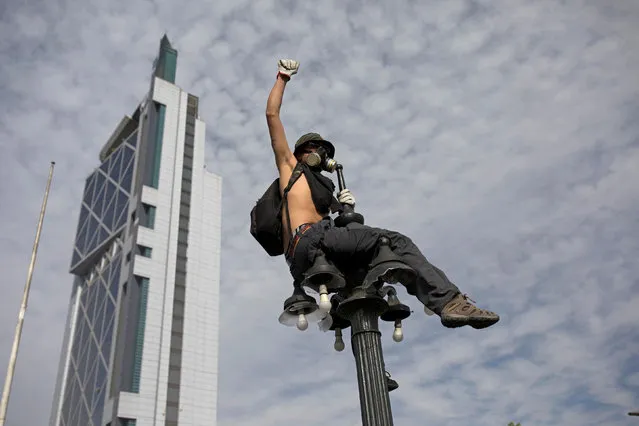 A demonstrator sits on a street light as protests against high living costs continue, in Santiago, Chile on October 22, 2019. (Photo by Pablo Sanhueza/Reuters)