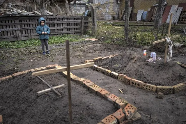 In the courtyard of their house, Vlad Tanyuk, 6, looks at the grave of his mother Ira Tanyuk, who died because of starvation and stress due to the war, in Bucha, on the outskirts of Kyiv, Ukraine, Monday, April 4, 2022. (Photo by Rodrigo Abd/AP Photo)