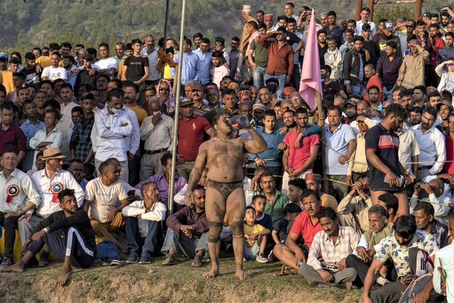 A wrestler drinks water standing among spectators as he gets ready for his next match at a local fair in Dharmsala, India, Tuesday, March 29, 2022. These local fairs, once an annual feature, are slowly returning after being cancelled during the COVID-19 pandemic. (Photo by Ashwini Bhatia/AP Photo)