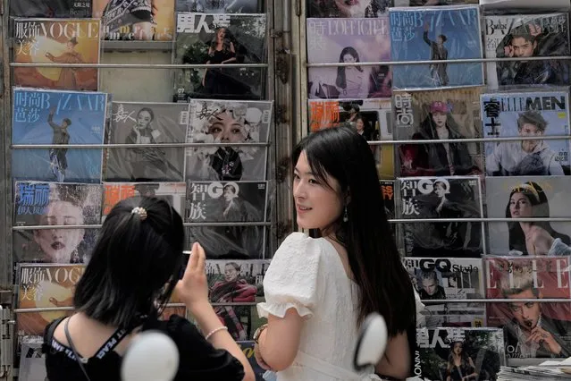 A woman poses for a photo near magazines showing celebrities at a newsstand in Beijing on August 1, 2021. Hugely popular online games and celebrity culture are the latest targets in the ruling Communist Party's campaign to encourage China's public to align their lives with its political and economic goals. (Photo by Ng Han Guan/AP Photo)