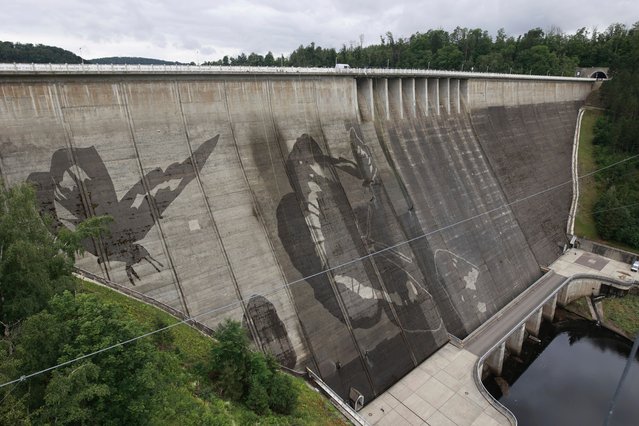 Industrial climbers help create graffiti by the artist Klaus Dauven by using a high-pressure cleaner to form a contrast between the cleaned and uncleaned surface of the dam wall at the Rappbode reservoir in Elbingerode, Germany on July 5, 2024. (Photo by Matthias Bein/AP Photo)