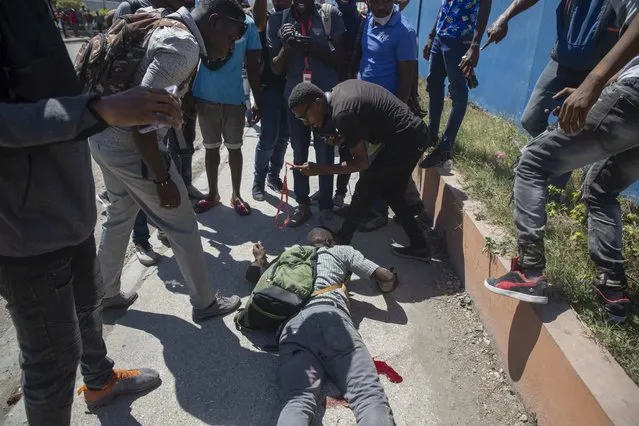 People stand around a man who was injured by gunfire during a protest by factory workers demanding higher salaries in Port-au-Prince, Haiti, Wednesday, February 23, 2022. (Photo by Joseph Odelyn/AP Photo)