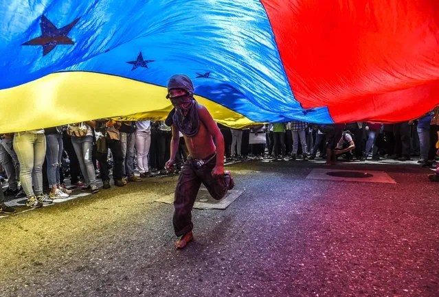 A boy runs under a Venezuelan flag during a protest of journalists and media workers against the attacks on journalists, in Caracas on June 27, 2017. (Photo by Juan Barreto/AFP Photo)