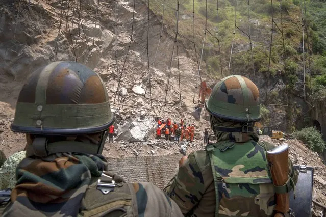 Indian army soldiers watch from a distance as earth movers dig through the rubble of a collapsed tunnel in Ramban district, south of Srinagar, Indian controlled Kashmir, Friday, May 20, 2022. An official in Indian-controlled Kashmir said Friday that 10 workers were trapped after part of a road tunnel collapsed in the Himalayan region. (Photo by Dar Yasin/AP Photo)