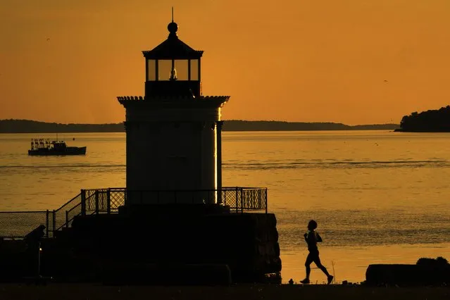 A jogger runs towards Bug Light while a lobster boat heads out of Portland Harbor under calm conditions, Tuesday morning. June 7, 2022, in South Portland, Maine. Southern Maine can expect a soaking rain on Wednesday. (Photo by Robert F. Bukaty/AP Photo)