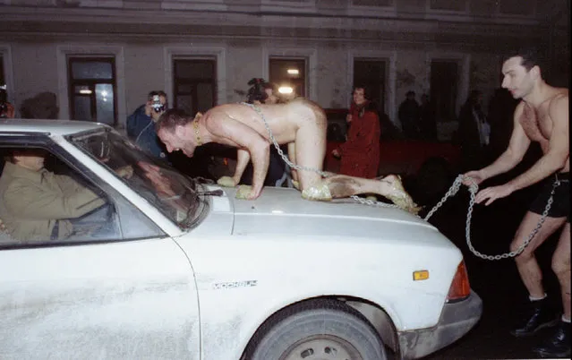 Russian artist Oleg Kulik imitating a dog, jumps on the car of a scared Muscovite as his colleague Alexander Brener, representing his owner, tries to hold him back during an exhibitionist action in the centre of Moscow on November 23, 1994. The artists staged the action protesting against modern Russian society. (Photo by Reuters/Stringer)