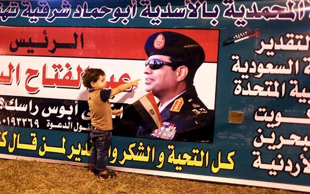A child points to a picture of President Abdel Fattah al-Sisi as he poses for picture while people gather to celebrate in Tahrir square in Cairo, Egypt, August 6, 2015. (Photo by Asmaa Waguih/Reuters)