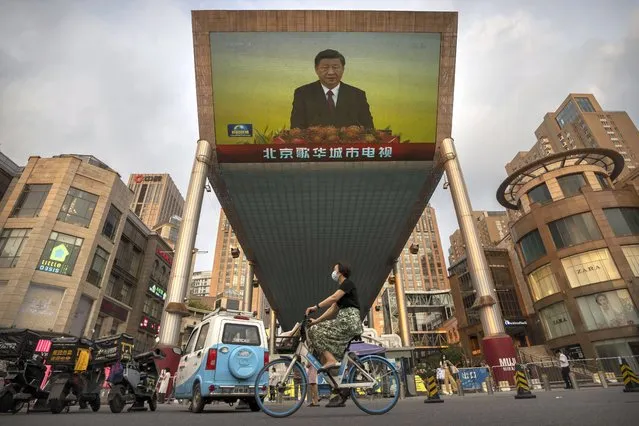 A woman wearing a face mask rides a bicycle past a large television screen at a shopping center displaying Chinese state television news coverage of Chinese President Xi Jinping's visit to Hong Kong in Beijing, Friday, July 1, 2022. China's leader Xi Jinping marked the 25th anniversary of Hong Kong's return with a speech Friday that emphasized Beijing's control over the former British colony under its vision of “one country, two systems” – countering criticism that the political and civic freedoms promised for the next quarter-century have been largely erased under Chinese rule. (Photo by Mark Schiefelbein/AP Photo)