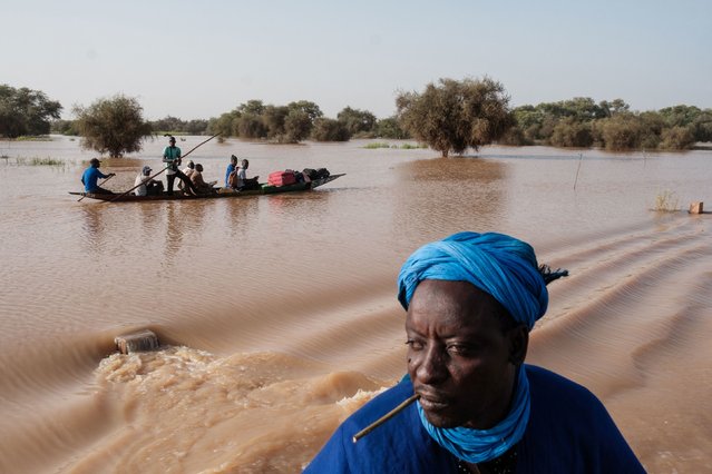 People carry possessions on a pirogue over flood water flowing over a main road in Odobere on October 22, 2024. Floods along the Senegal river have affected over 55,000 people after heavy rain in the Senegal River Basin leaving many villages underwater and over 1,000 hectares of farm land submerged. (Photo by Guy Peterson/AFP Photo)