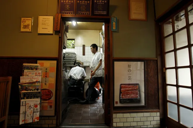 In this August 2, 2017 photo, men in the kitchen busily prepare for dinner service at Hashimoto, a Michelin one-star unagi restaurant in Tokyo. The unagi restaurant first opened in 1853 and is now in its sixth-generation. Many locals order unajyu, pictured in the posters on the wall, and can eat in or have it prepared for take-away. The restaurant uses only farmed eels, which tend to be larger and fattier than wild eels. The endangered Japanese summer delicacy may get a new lease on life with commercial farming. (Photo by Sherry Zheng/AP Photo)