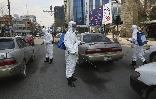 Volunteers in protective suits spray disinfectant on passing vehicles helping curb the spread of the coronavirus in Kabul, Afghanistan, Sunday, March 29, 2020. The government Friday ordered a three-week lock-down for Kabul to stem the spread of the new coronavirus. (Photo by Rahmat Gul/AP Photo)